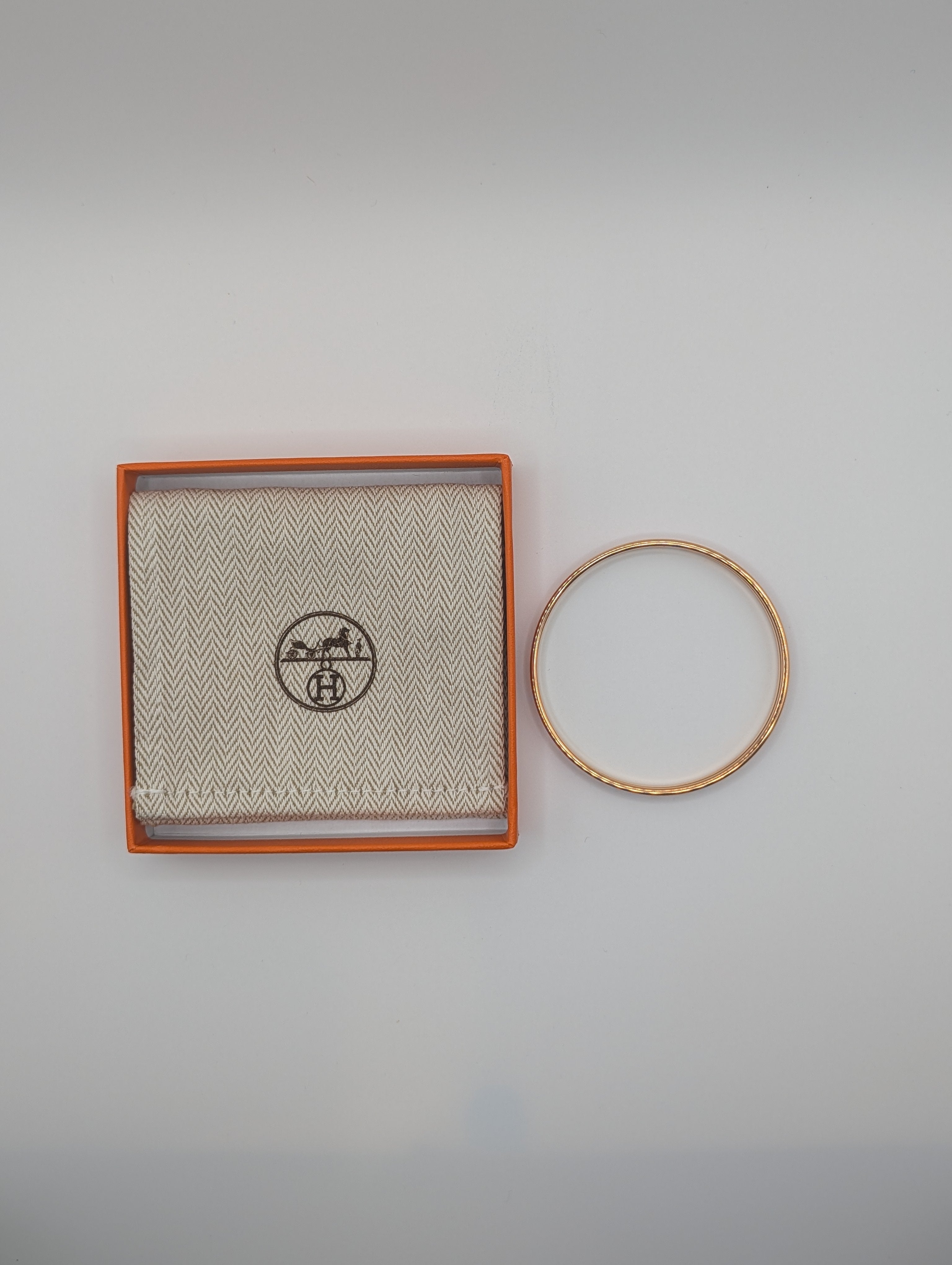 Gold bracelet on a gray background with a branded box.