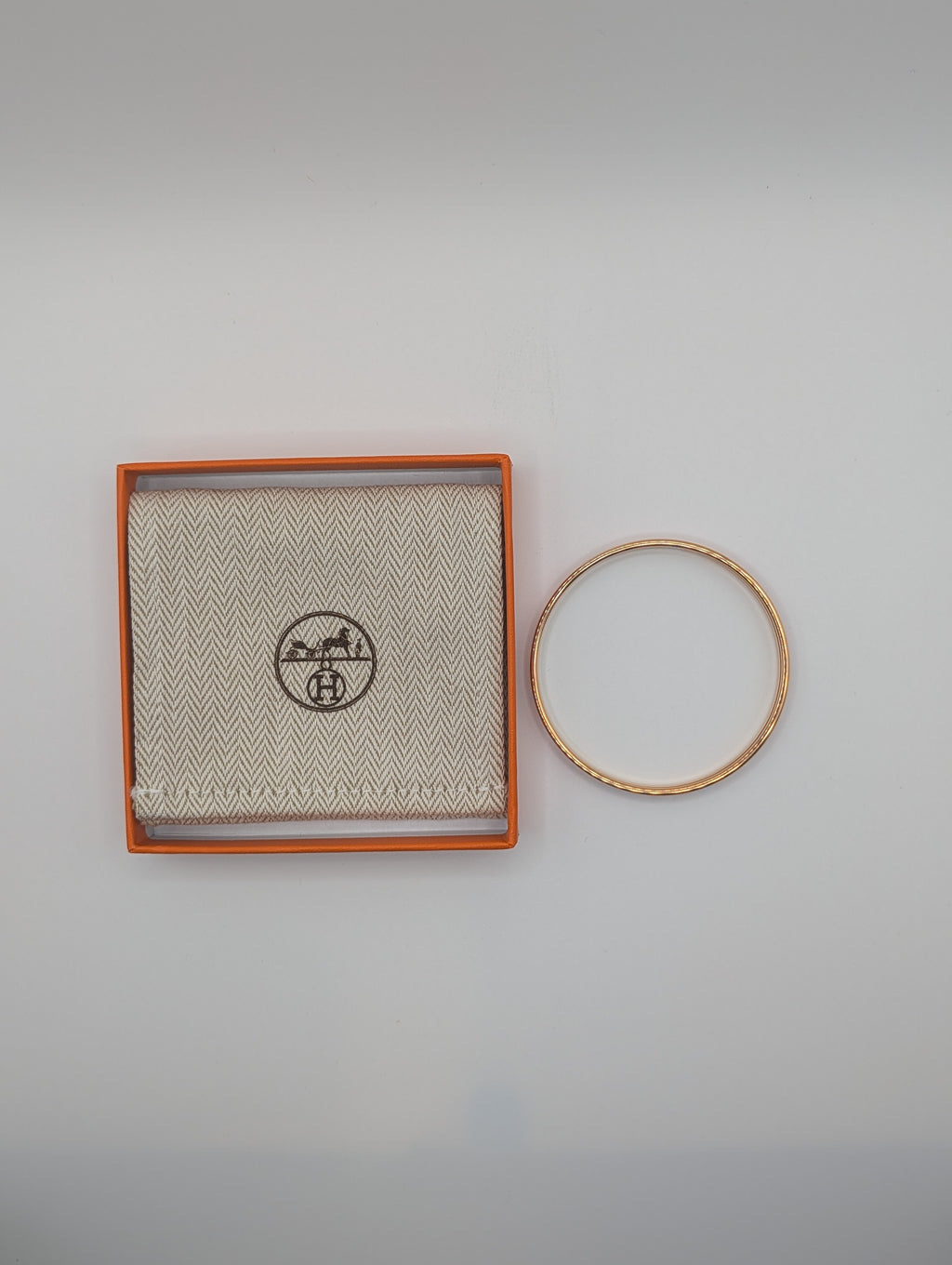 Gold bracelet on a gray background with a branded box.