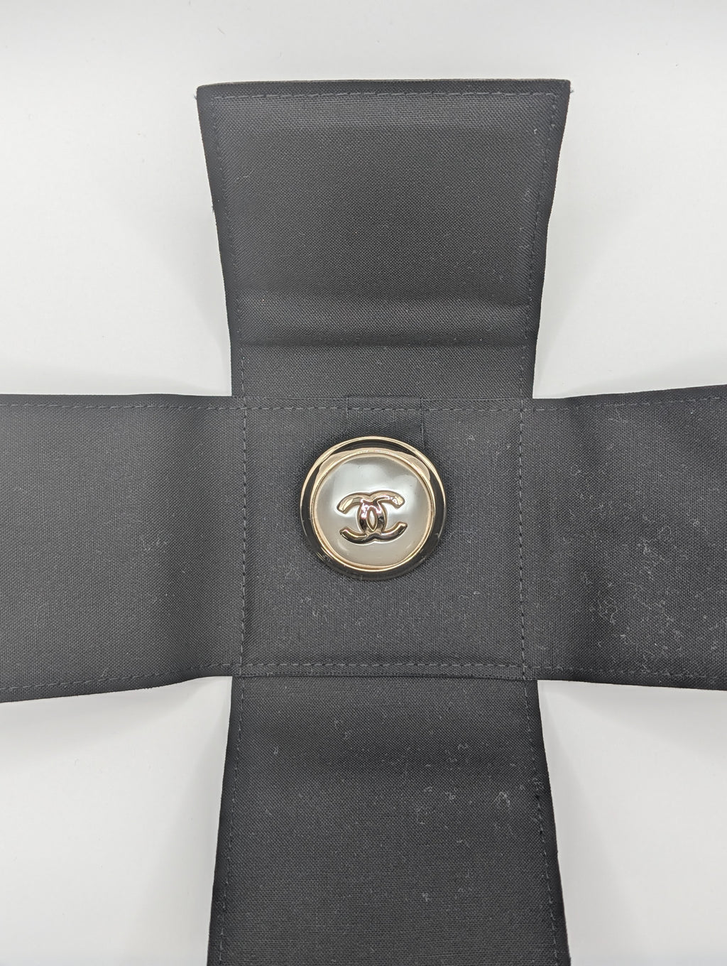 Gray cross-shaped pillow with a button featuring a logo on a white background