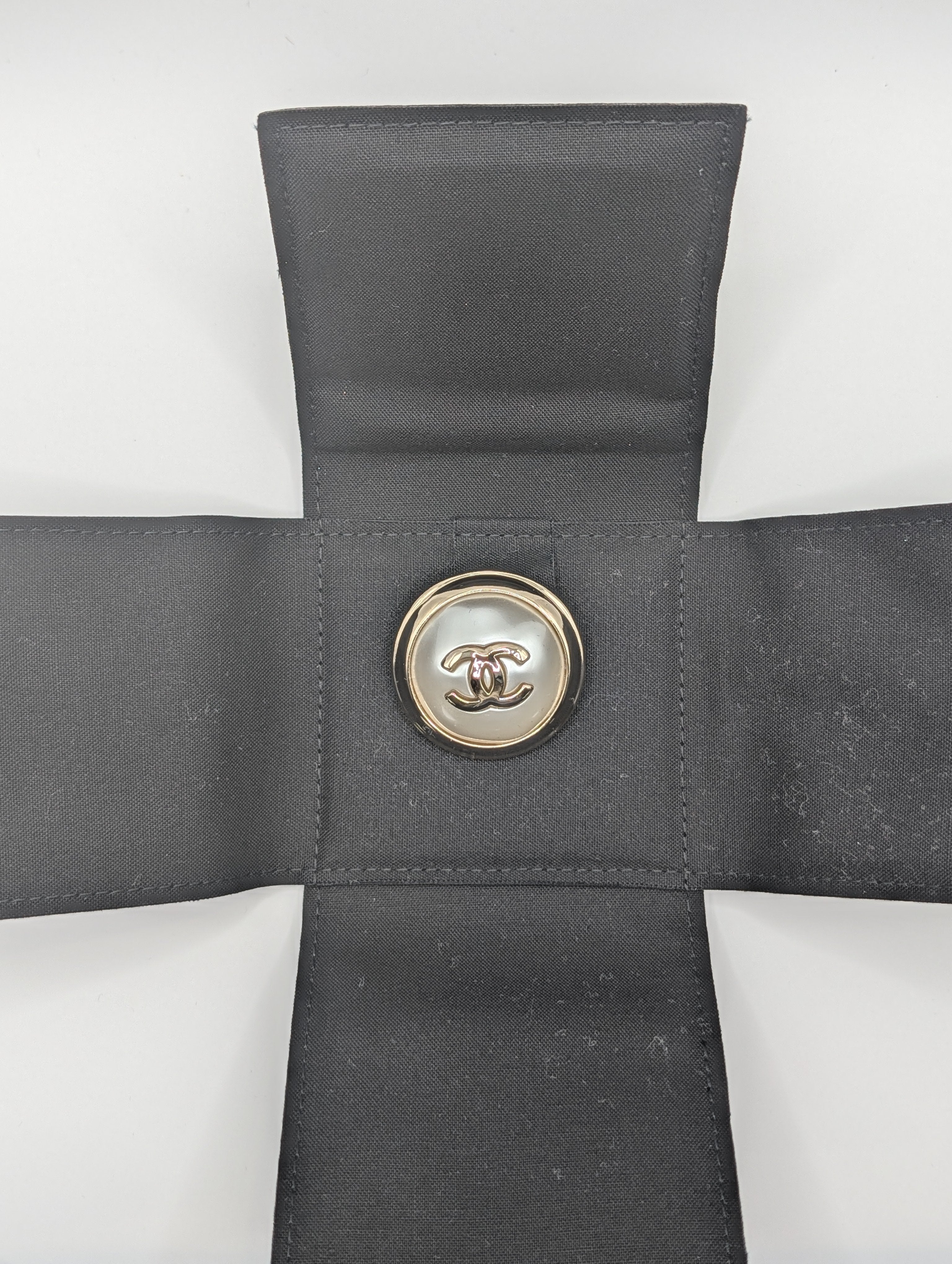Gray cross-shaped pillow with a button featuring a logo on a white background