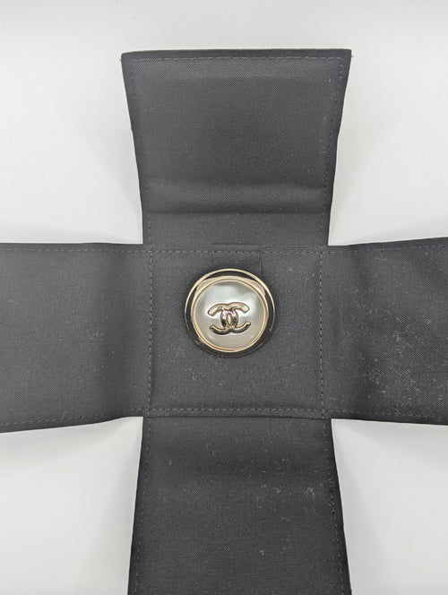Gray cross-shaped pillow with a button featuring a logo on a white background